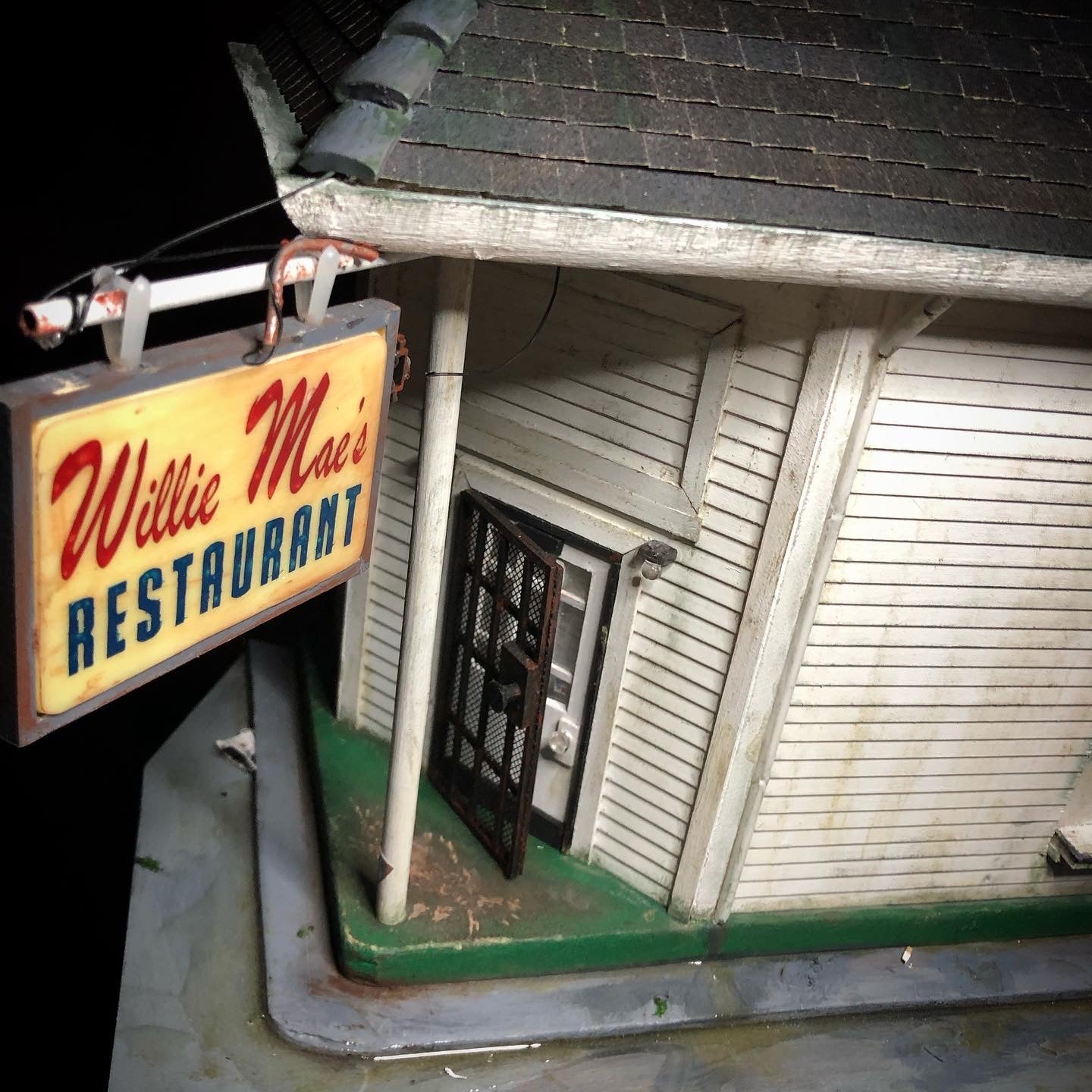 Another photo of Willie Mae's miniature model, this photo shows the front door from the front at an elevated angle looking down, there is a metal security door and the door is slightly ajar.