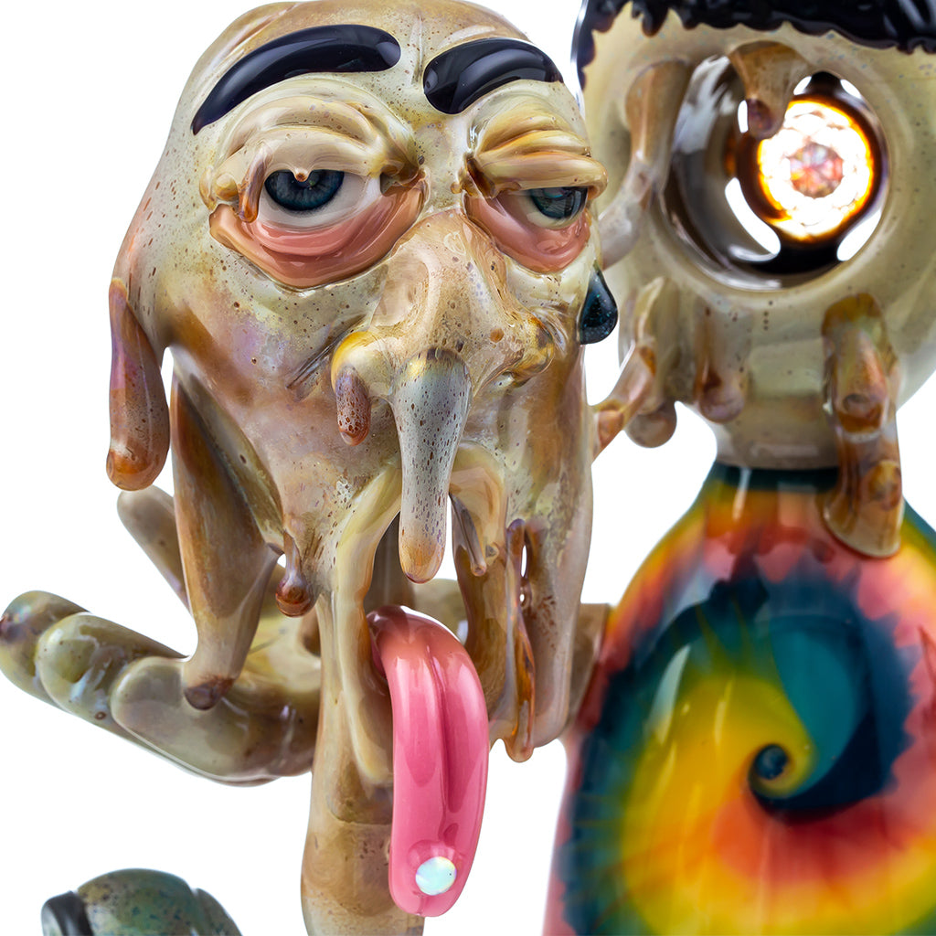 Close up studio photo of a R3G15 Heady Glass Piece, piece has a dripping face with opal lsd tab on tongue and tie dye shirt. 