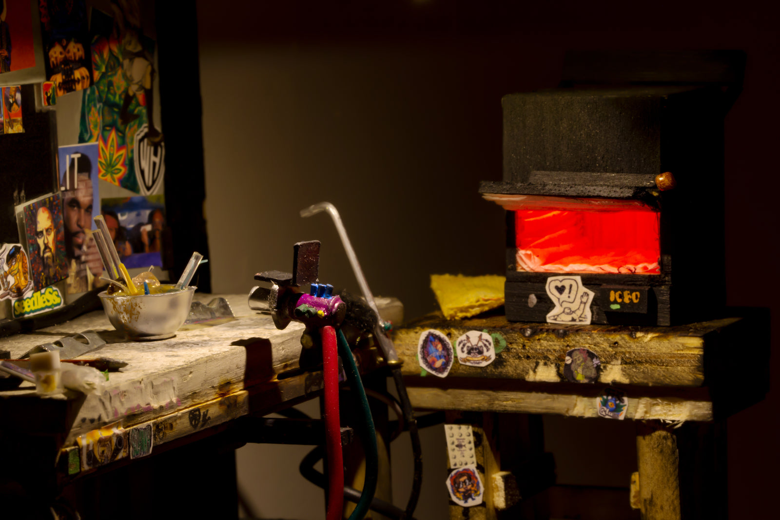 Miniature glass blowing station with torch, kiln, water bowl, mirror at back of station, and stickers on basically everything. 
