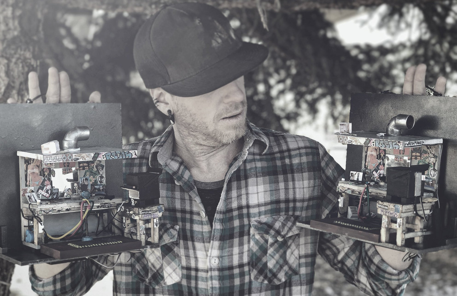 R3G15 shown holding two miniature glassblowing stations, one in either hand. The models are mounted on boards and have handles at the top to hold or hang them from which R3G15 is holding them from.